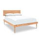 A Larssen Bed by Vermont Furniture Designs with a simple headboard, supporting a mattress with white bedding and two pillows, features a natural cherry finish. The bed is isolated on a white background.