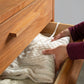 A person folding a white cable-knit sweater and placing it neatly inside an open drawer of the Vermont Furniture Designs Loft 5-Drawer Chest, showcasing Vermont craftsmanship.