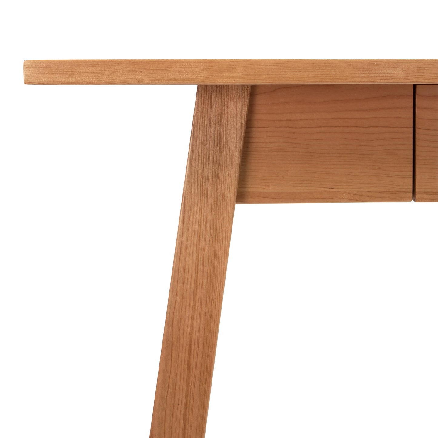 Alt text: Close-up of Vermont Woods Studios Manchester Writing Desk in sustainable solid wood, showcasing the edge of the tabletop, a support leg, and part of a drawer. This American-made writing desk features a smooth natural finish with visible grain patterns, ideal for modern home offices.