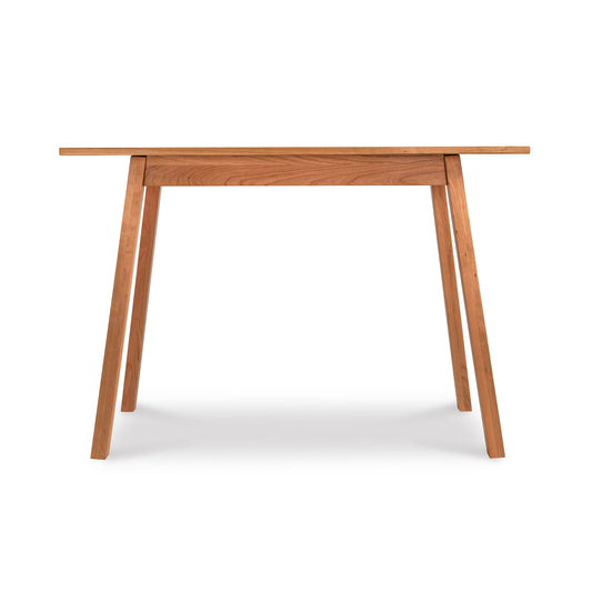 Alt text: Manchester Compact Desk in light brown wood featuring minimalist design from Vermont Woods Studios. Solid wood desk with rectangular top, four angled legs, and clean natural finish, perfect for home office or small spaces. American made furniture set against a white background.