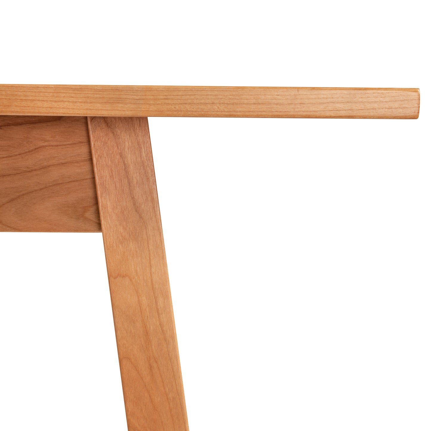 Close-up view of the Vermont Woods Studios Manchester Compact Desk in solid wood. The image highlights the junction where the light brown, smoothly finished tabletop meets the sturdy wooden leg. Showcasing expert craftsmanship and American made quality furniture.