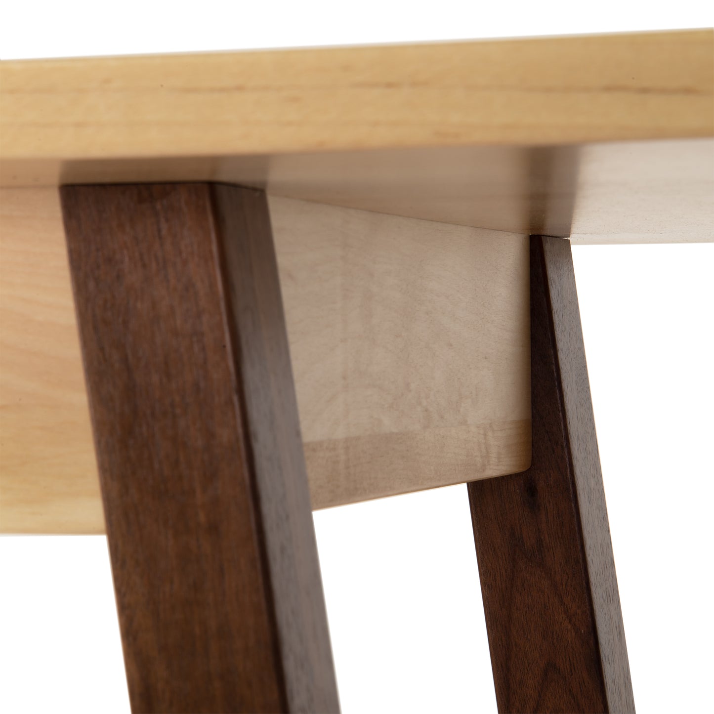 Alt text: Close-up view of a solid wood table corner, featuring a light cherry wood tabletop and dark walnut wood legs angled inward. This image highlights the detailed craftsmanship and modern design of the Manchester Two-Tone Compact Desk by Vermont Woods Studios, ideal for contemporary 21st-century homes.