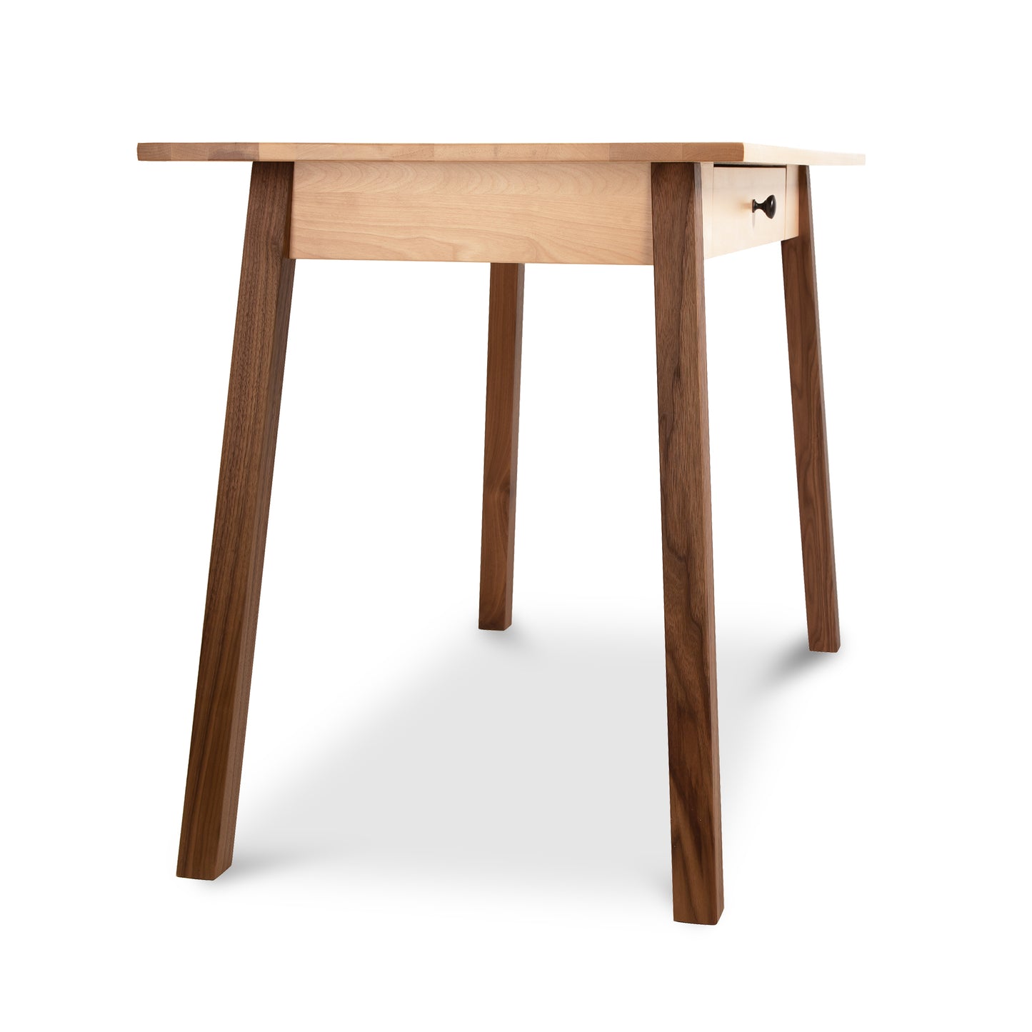 A Manchester Two-Tone Writing Desk, crafted from sustainable solid wood, with a light-colored tabletop and four dark brown legs, isolated on a white background. The desk design includes a small, visible drawer with a knob. Brand: Vermont Woods Studios