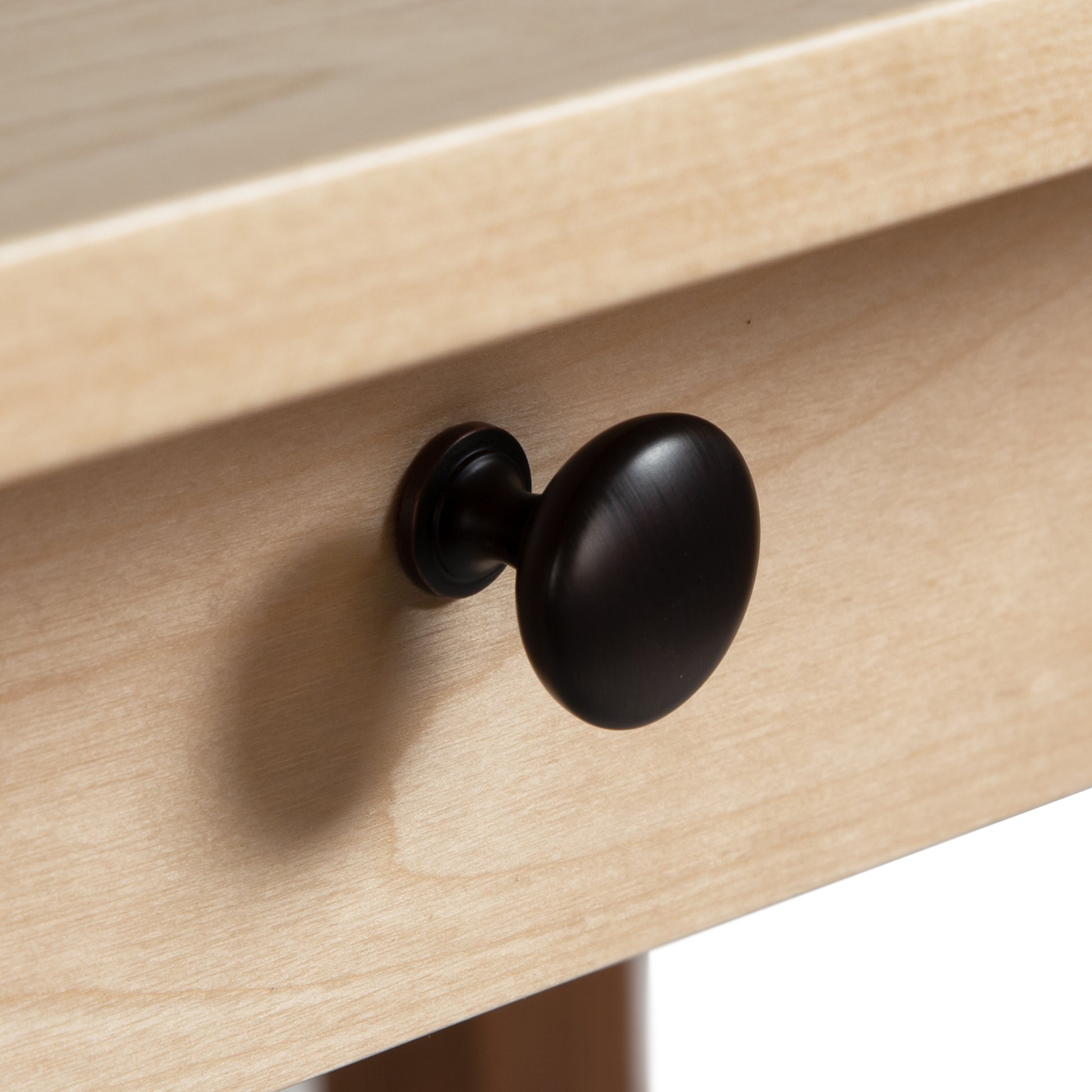 Close-up of a round, black metal drawer knob attached to a sustainable solid wood Vermont Woods Studios Manchester Two-Tone Writing Desk, casting a soft shadow on the drawer front.
