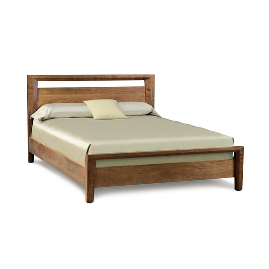 A neatly made Mansfield Walnut Platform Bed by Copeland Furniture with a cream-colored mattress and pillow on an isolated background.
