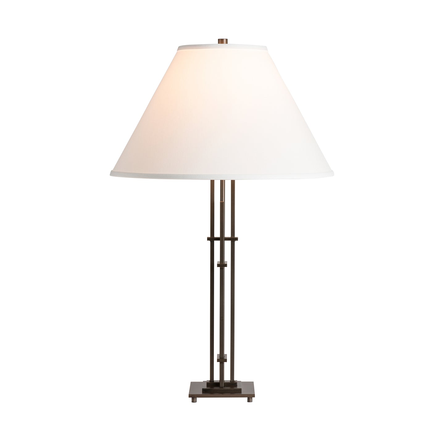 A Hubbardton Forge Metra Quad Table Lamp with a white cone-shaped shade and a hand-forged wrought iron base featuring vertical rod support. The lamp is illuminated and set against a plain white background.