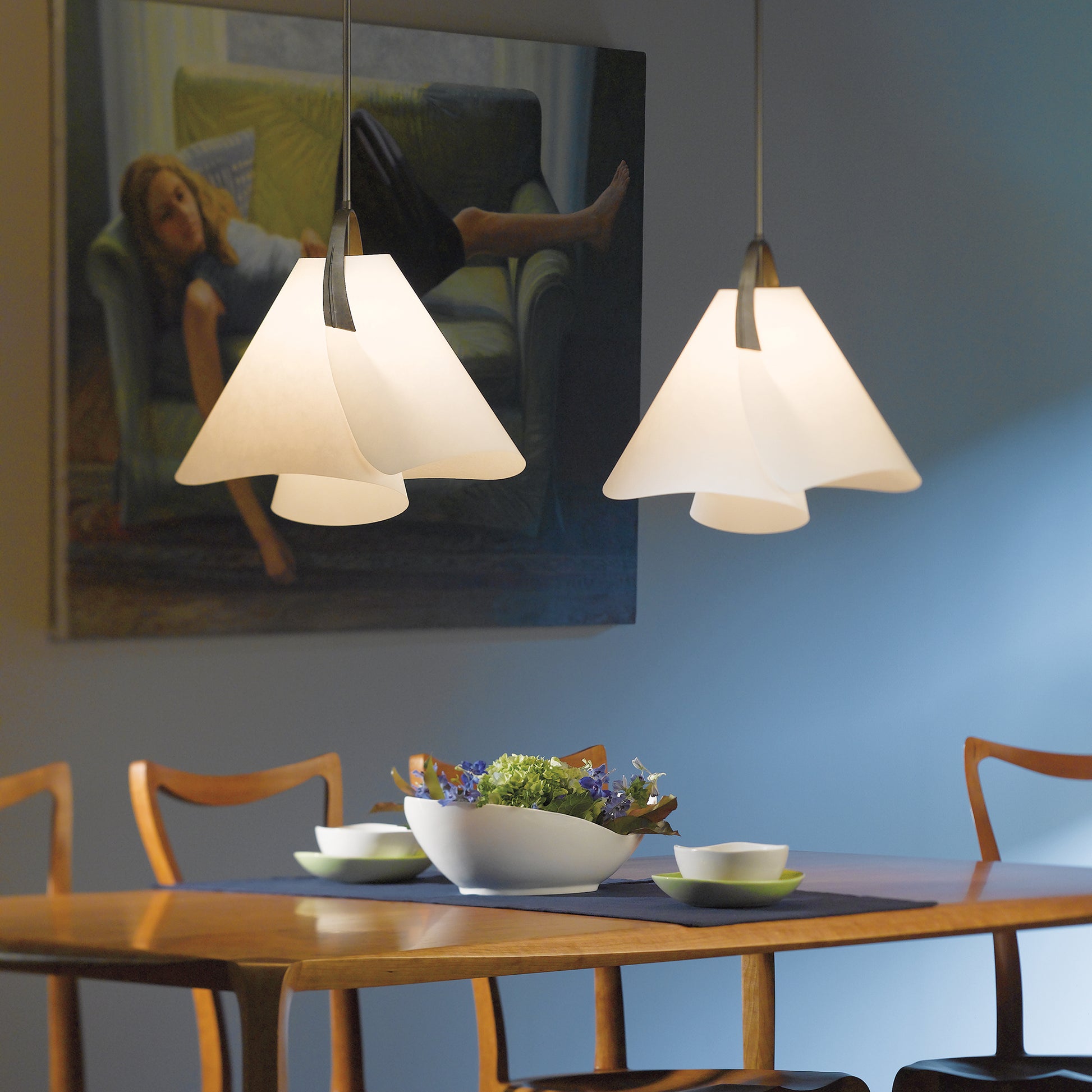 Wooden dining table with three chairs, highlighted by hanging Mobius Small Pendants, featuring a decorative bowl centerpiece.