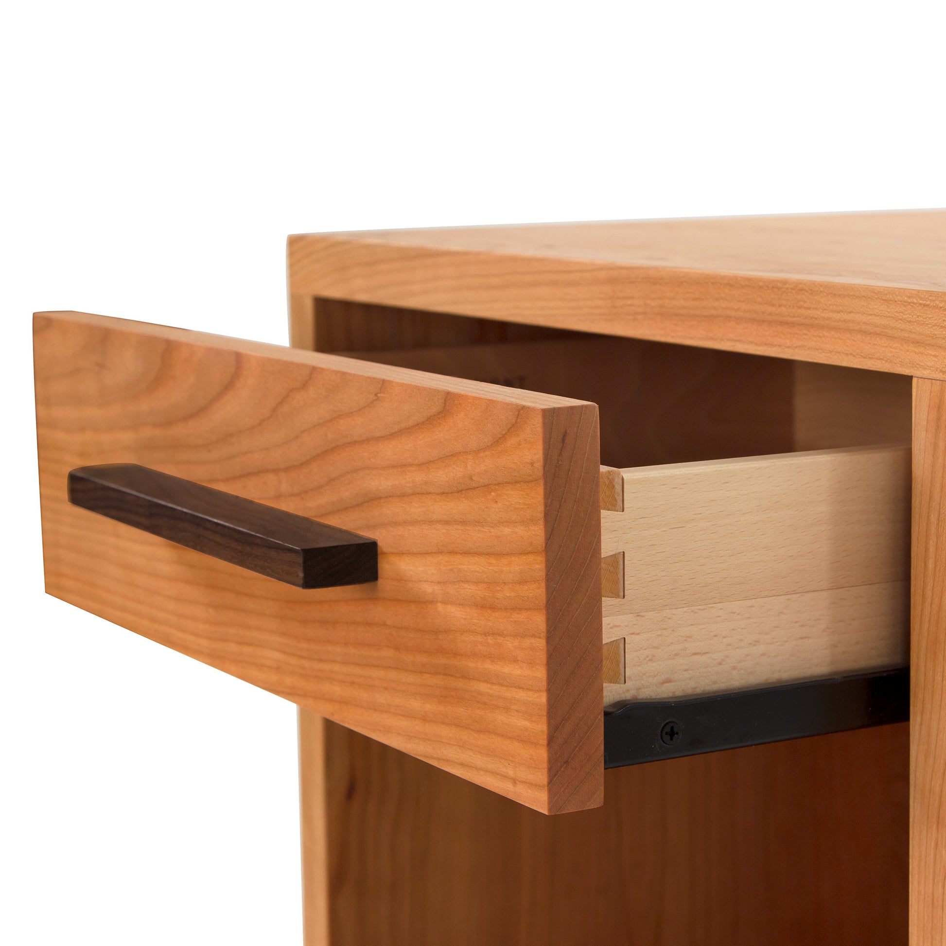 A close-up view of an open Vermont Furniture Designs Modern American 1-Drawer Enclosed Shelf Nightstand featuring a dovetail joint, highlighting intricate craftsmanship and a dark wood handle against a white background.