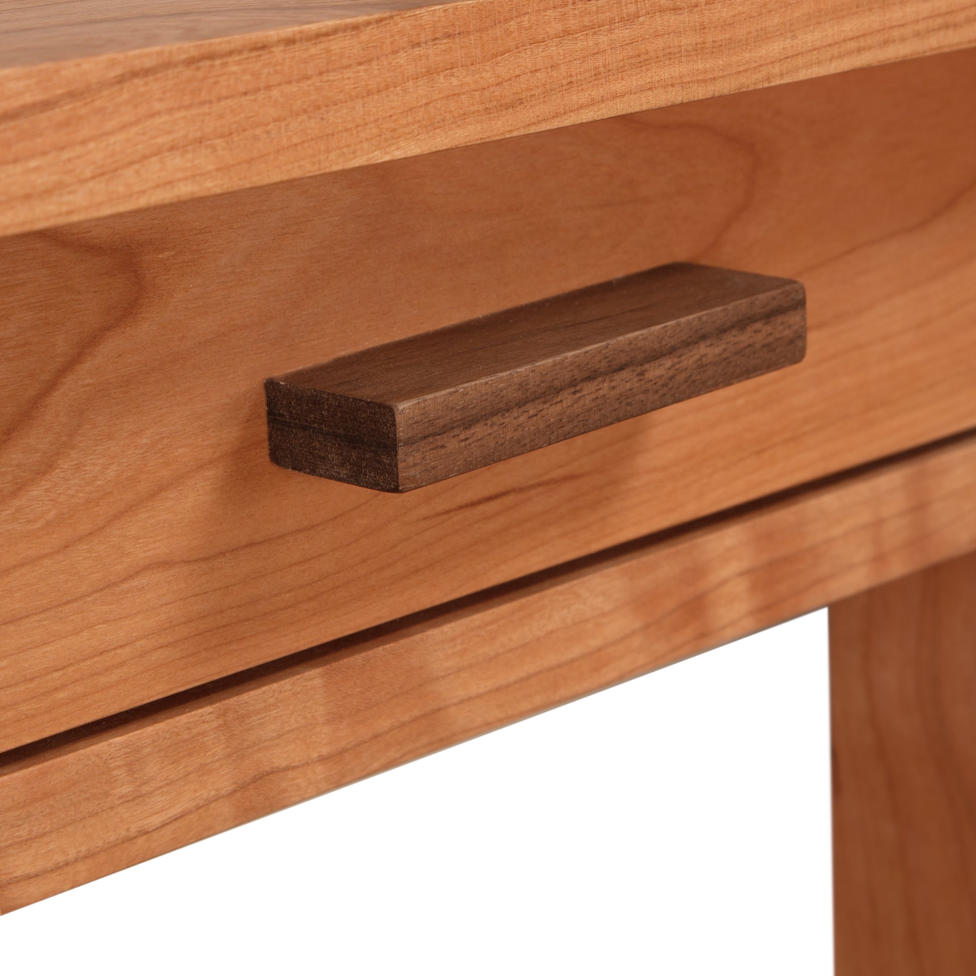 Close-up of a natural cherry wooden drawer with a simple rectangular pull handle, embodying Vermont Furniture Designs' Modern Craftsman Nightstand aesthetics.