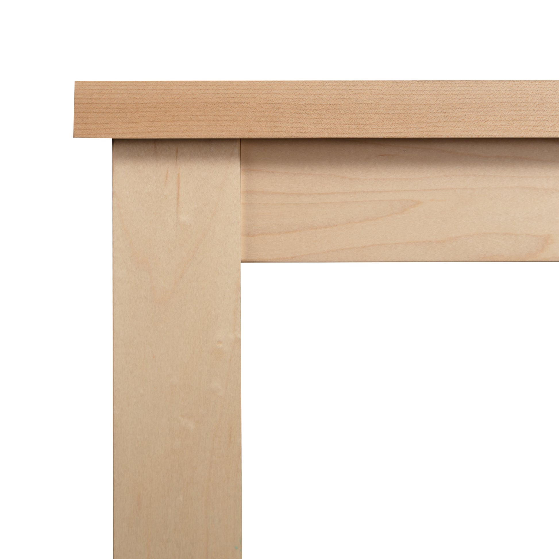 A close-up view of the corner of a Modern Mission Parsons Solid Top Table - Maple - 36"x48" - Clearance by Lyndon Furniture, handcrafted in Vermont. The image showcases the junction between the tabletop and table legs, emphasizing the smooth, natural wood grain and simple, clean lines of this eco-friendly design.