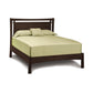 A solid cherry wood Monterey Platform Bed frame with a dark finish, complete with light green eco-friendly bedding that includes a fitted sheet, top sheet, two pillows, and a matching pillowcase by Copeland Furniture.