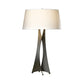 A modern Moreau Table Lamp from Hubbardton Forge with a unique, tripod-like base in wrought iron and a large, cylindrical white shade, isolated on a white background.
