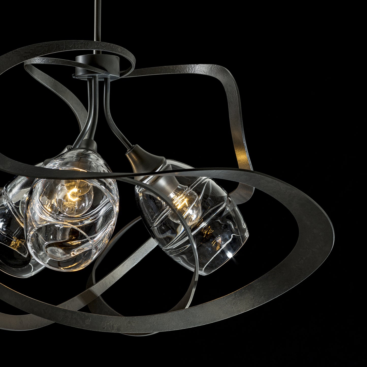 A modern Nest Pendant by Hubbardton Forge with swirling metal arms and clear glass bulbs, showcasing exquisite handcrafted design.