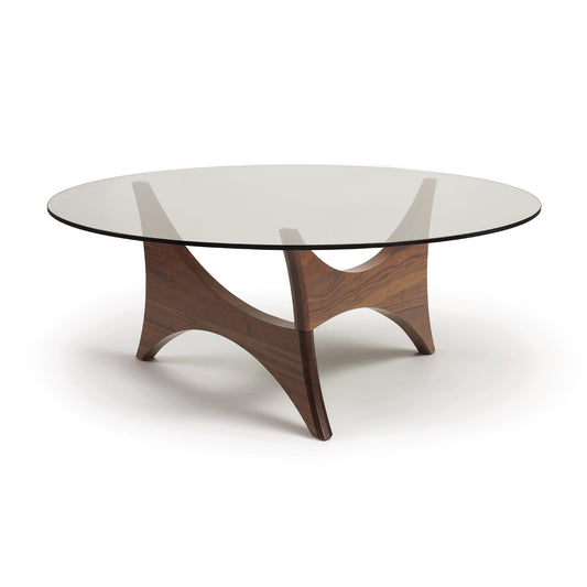 A Copeland Furniture Pivot Round Coffee Table with a walnut wooden base and tempered glass top on a white background.