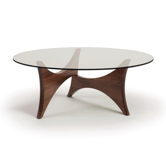 Pivot Round Coffee Table by Copeland Furniture with a glass top and sculpted walnut base, showcasing three elegant curved legs.