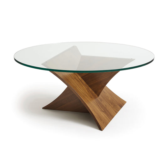 A modern Planes Round glass-top coffee table with a walnut wood base designed as a sculptural artform with intersecting planks by Copeland Furniture.