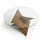 A modern Copeland Furniture Planes Round Glass Top Coffee Table with a tempered glass top resting on a wooden base shaped like a three-dimensional star.