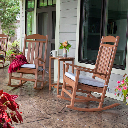 Pair of POLYWOOD Presidential Outdoor Rocking Chairs with gray cushions, highlighting their sturdy, American-made design and comfort. Small table beside them.