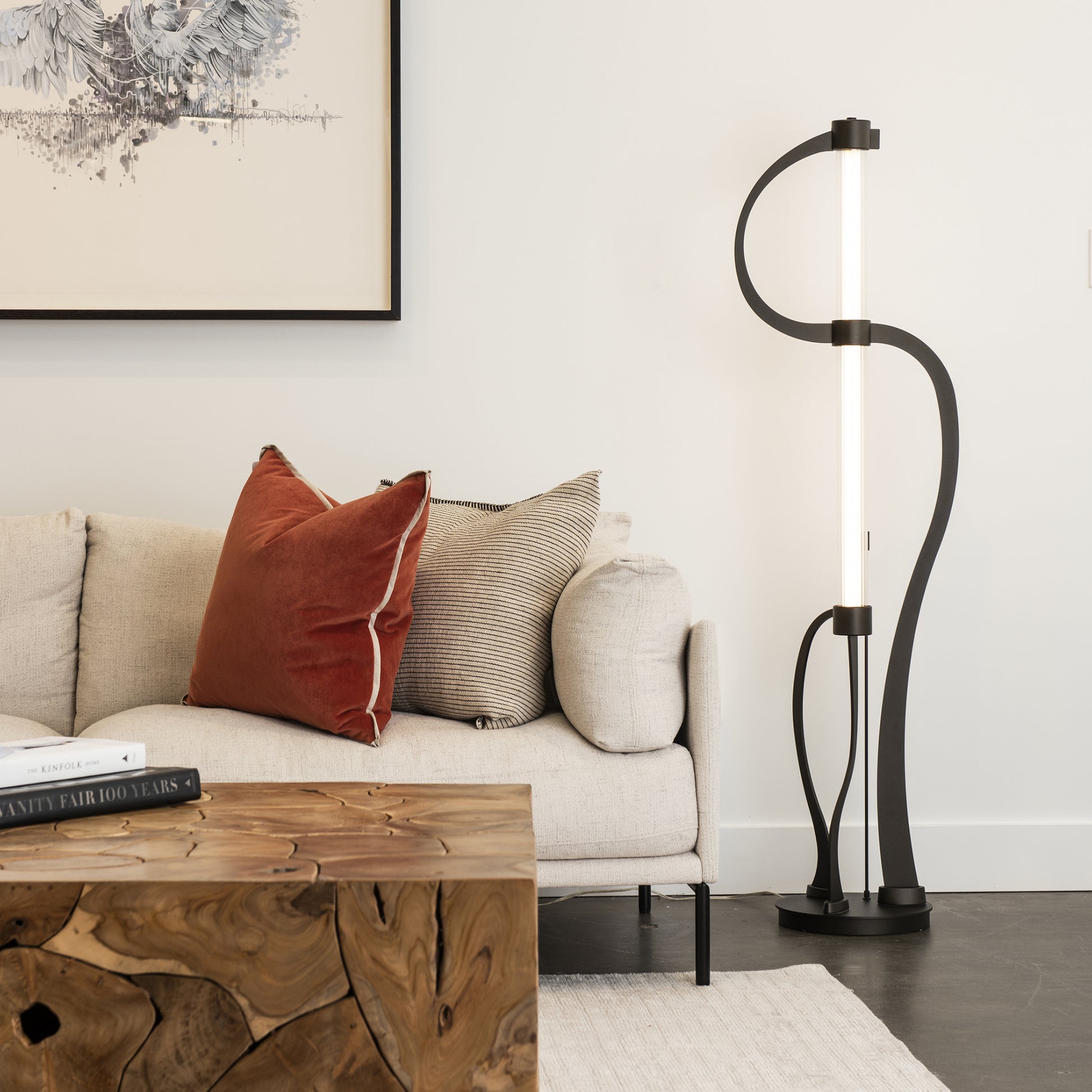Beige sofa with red and striped pillows, Pulse Floor Lamp by Hubbardton Forge, and wooden coffee table.