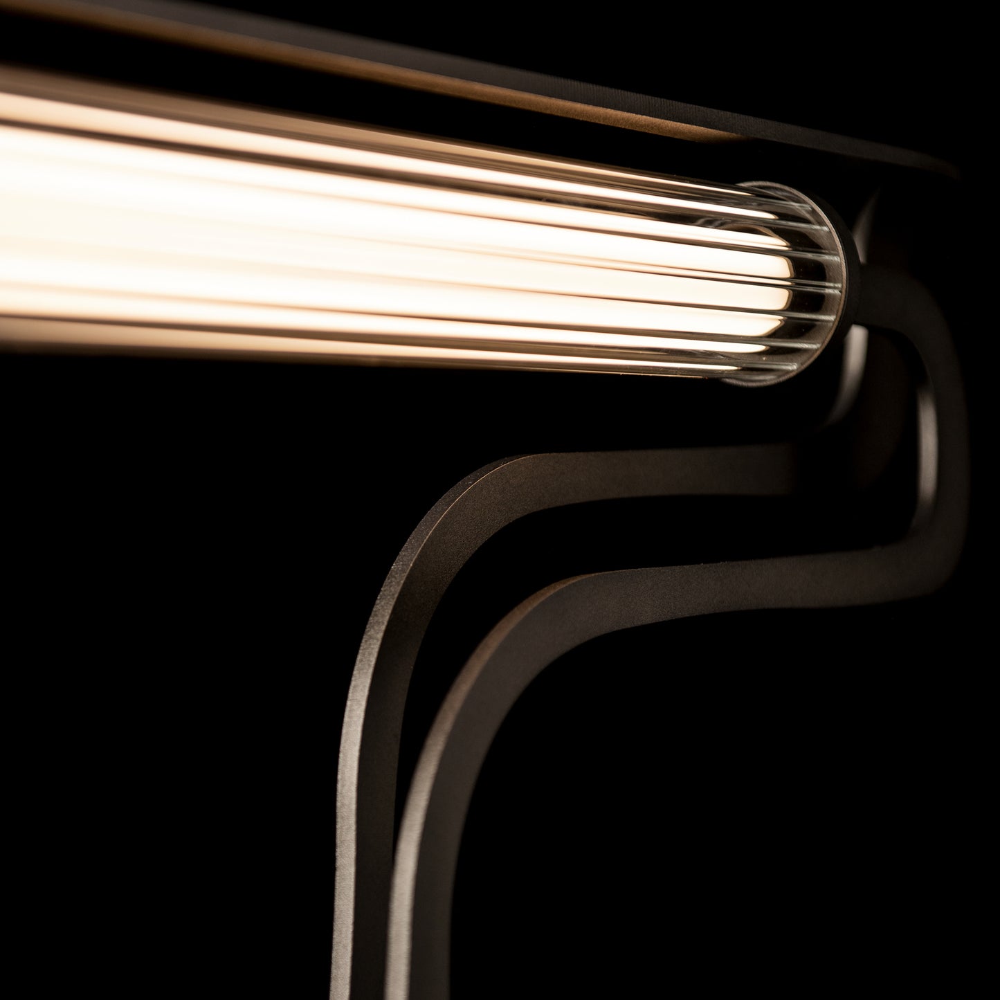 Hubbardton Forge Pulse Table Lamp featuring a glowing horizontal tube with curved black metal supports.