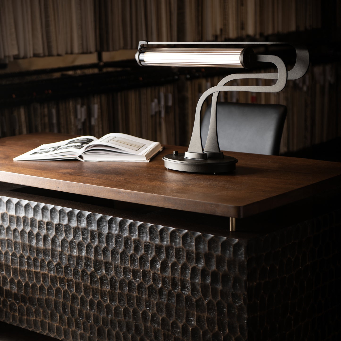 Hubbardton Forge Pulse Table Lamp in oil-rubbed bronze illuminates a wooden desk.