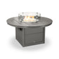 A round, gray POLYWOOD Round 48" Fire Pit Table outdoor fire pit table with a central flame under a clear glass wind guard on a plain white background.