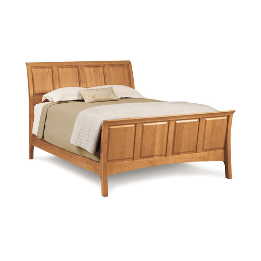 A solid cherry wood Sarah High Footboard Sleigh Bed with a headboard, complete with pillows and a beige bedspread, set against a white background. Brand Name: Copeland Furniture.