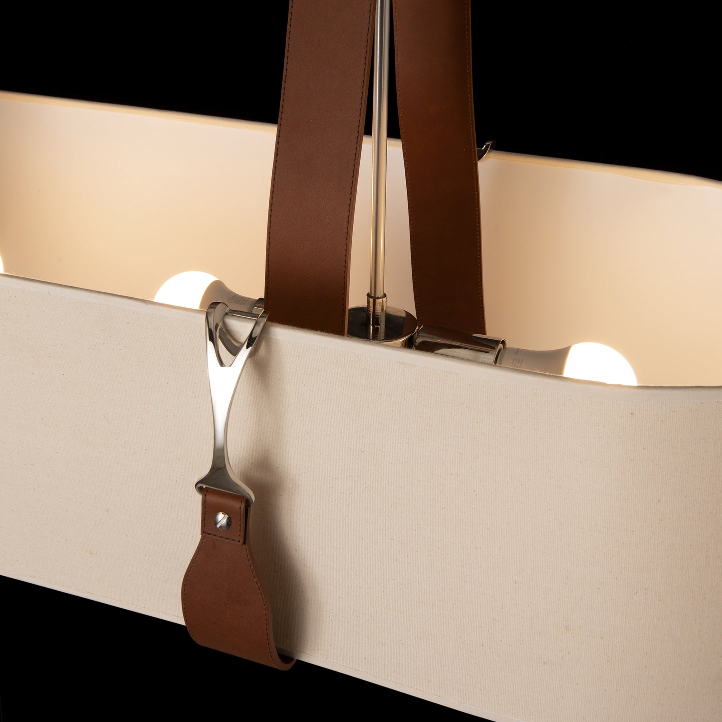Saratoga Oval Pendant by Hubbardton Forge with a beige shade and brown leather straps showcasing exposed bulbs.