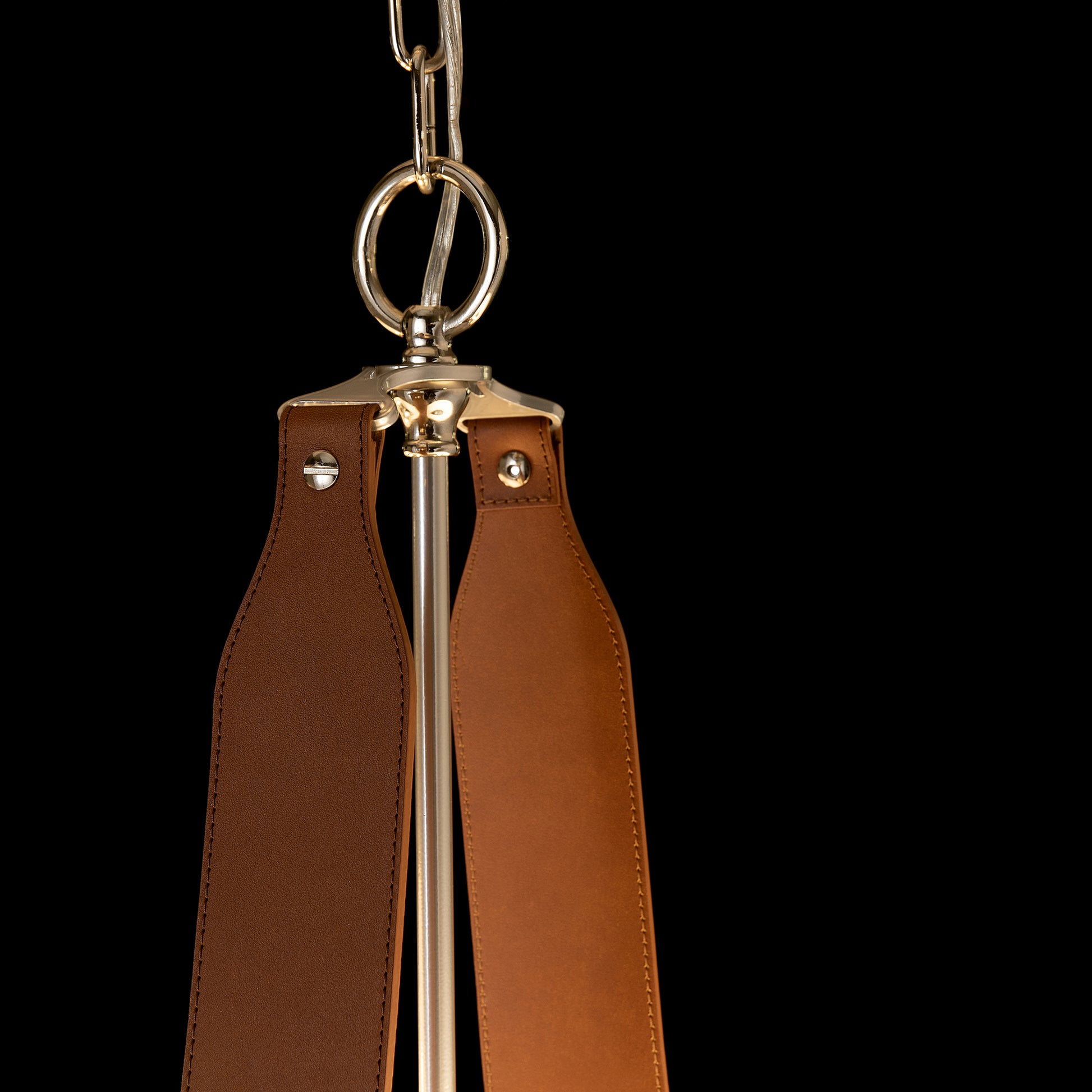 A close-up of a brown leather keychain with two straps, metal rivets, and a silver Saratoga Oval Pendant against a black background by Hubbardton Forge.