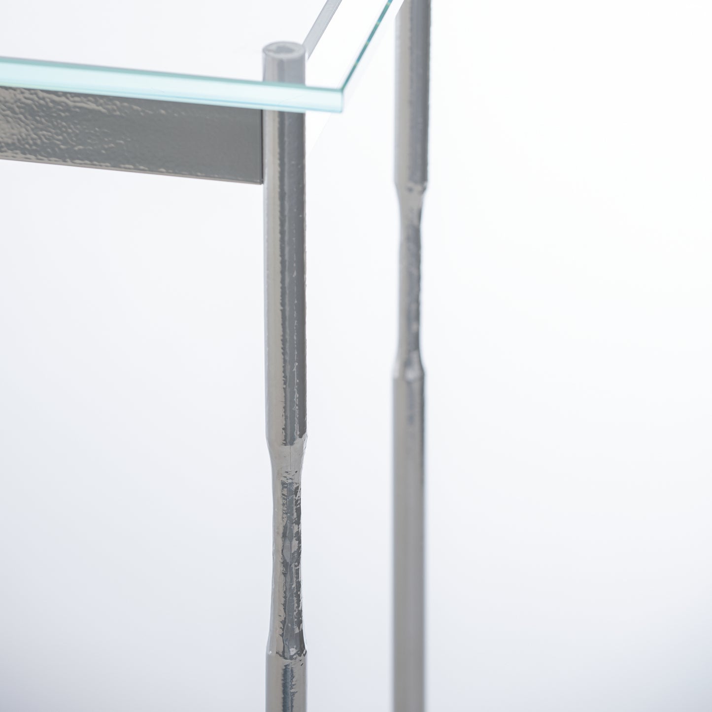 Senza Console Table by Hubbardton Forge featuring a textured leg, tempered glass top, and handcrafted silver steel frame.