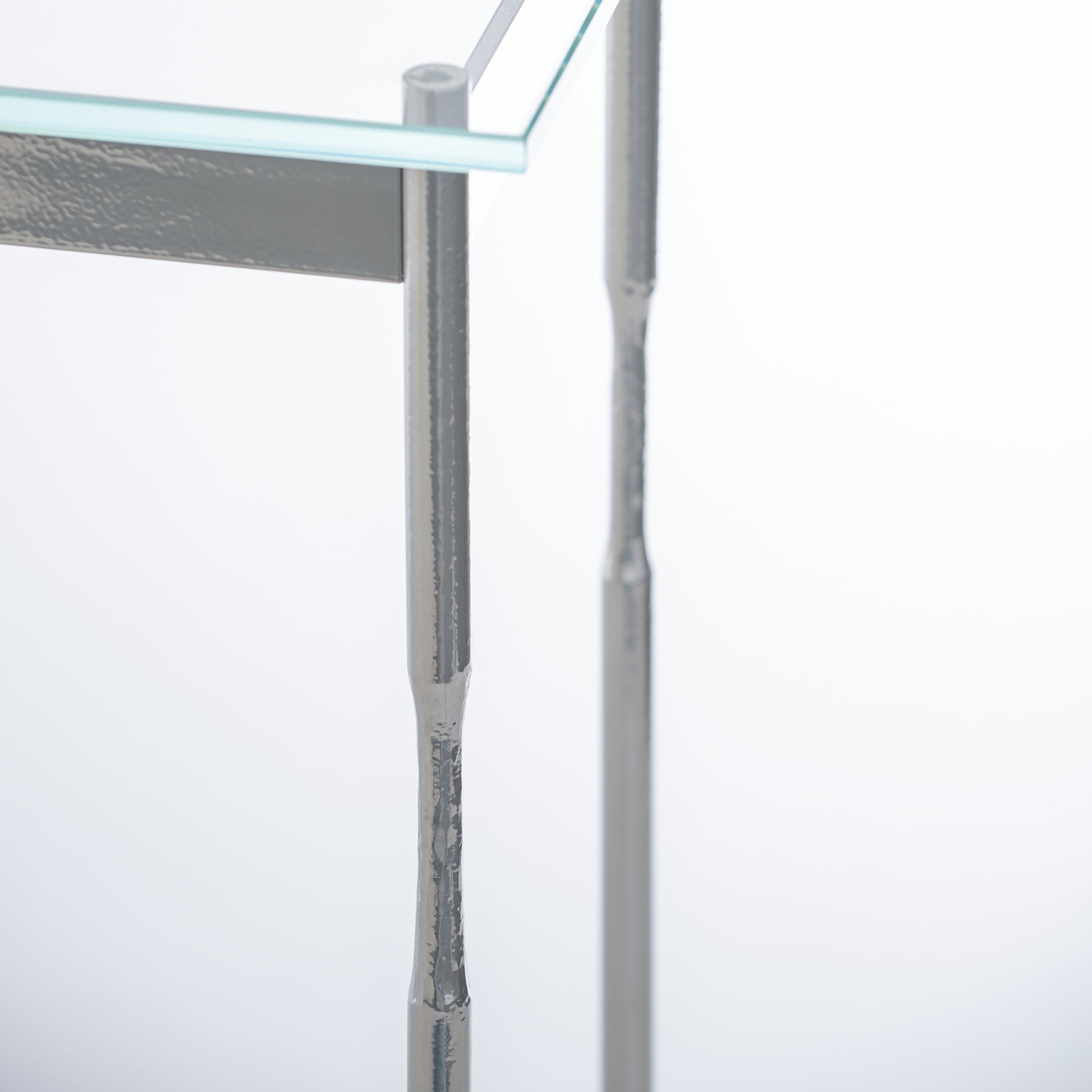 Senza Console Table by Hubbardton Forge featuring a textured leg, tempered glass top, and handcrafted silver steel frame.