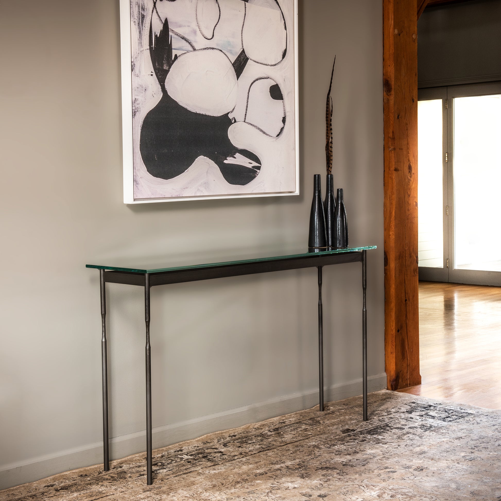 A Hubbardton Forge Senza Console Table with a tempered glass top in a room with a painting on the wall.