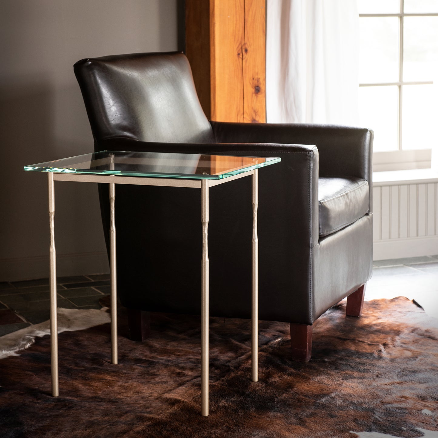 Black leather armchair paired with Hubbardton Forge Senza Side Table, featuring sleek metal legs, showcasing modern design and craftsmanship.