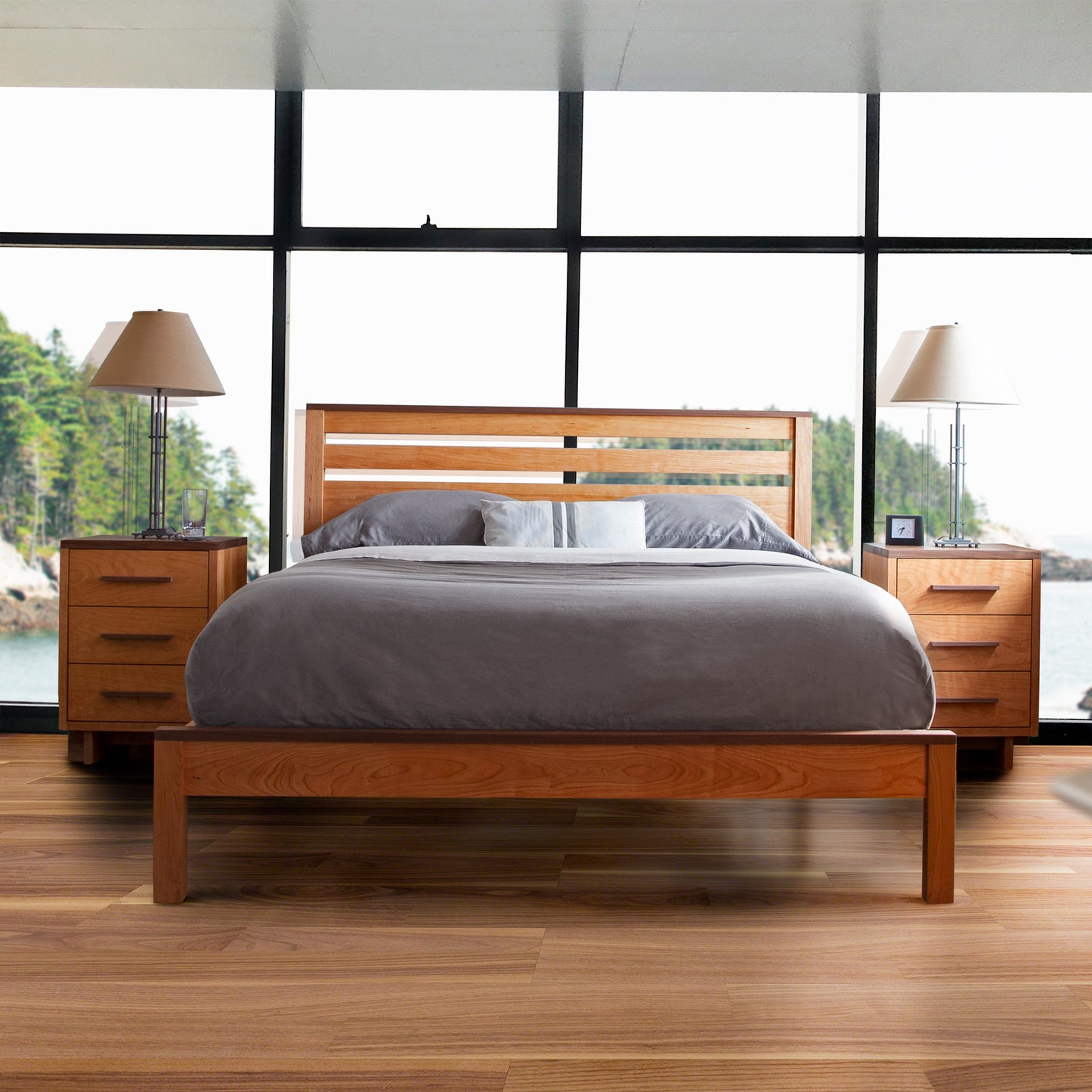 A modern eco-friendly bedroom with a solid Skyline Panel Bed by Vermont Furniture Designs and matching side tables, set against large windows overlooking a forested lakeside.