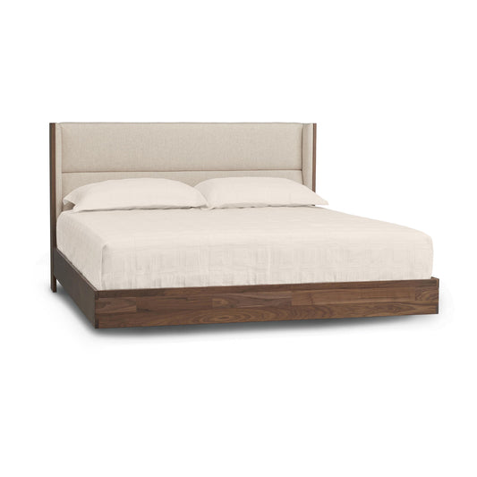 A modern Copeland Furniture Sloane Floating Bed with a dark wooden frame and beige upholstered headboard, equipped with white bedding and two pillows.