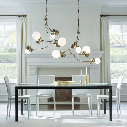 Black modern dining table with sleek white chairs set under elegant Hubbardton Forge Sprig Pendant lighting.