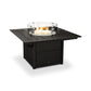 A POLYWOOD Square 42" Fire Pit Table with a visible flame, surrounded by a glass wind guard, set against a white background. The table features a dark finish and a lower shelf storage compartment.
