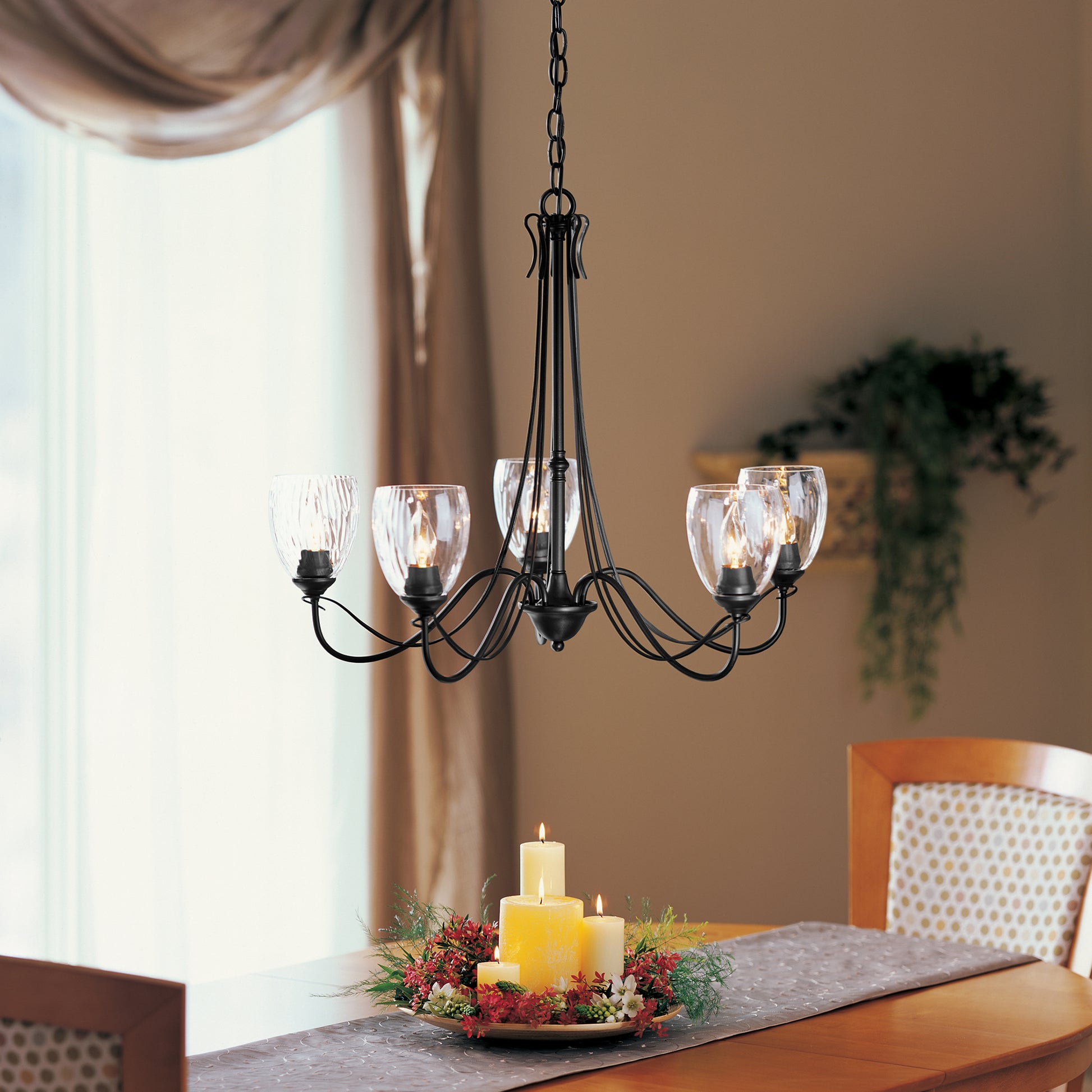 A dining room table with a Trellis 5-Arm Chandelier featuring a bronze finish from Hubbardton Forge.