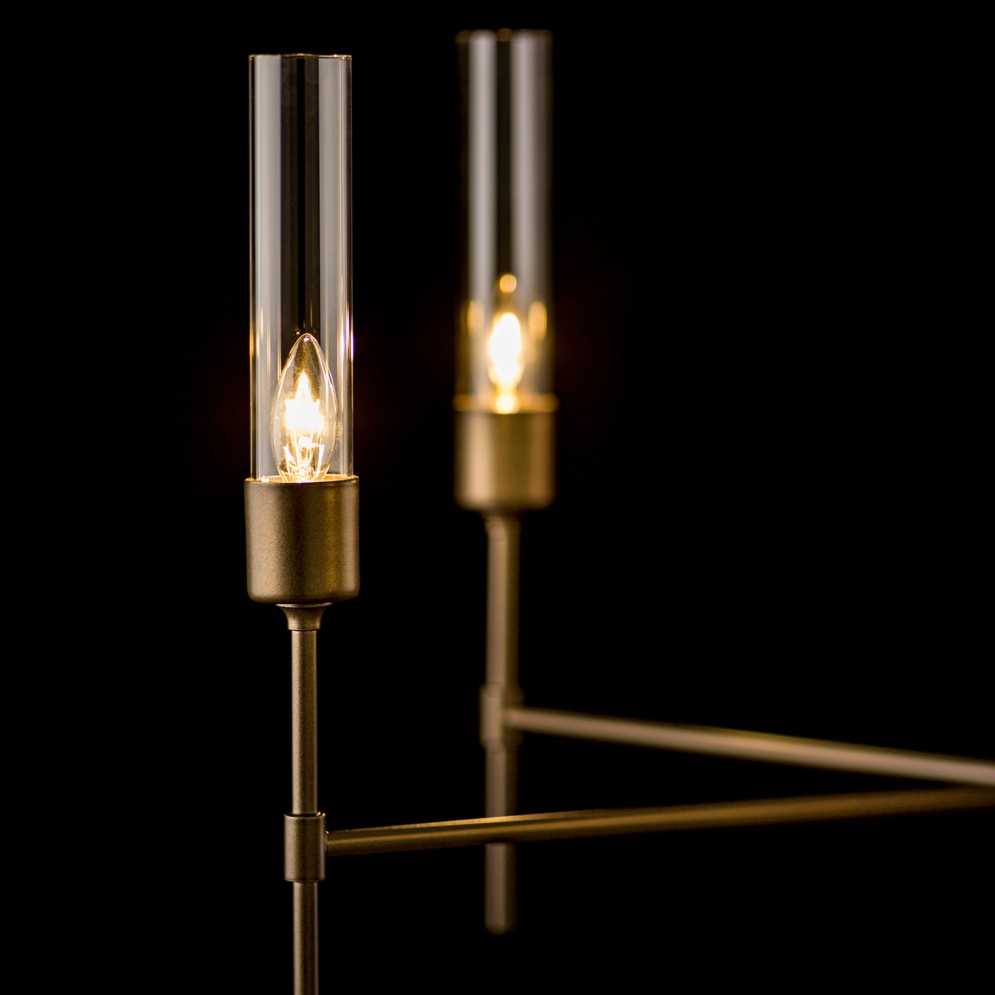 Hubbardton Forge Vela 5-Arm Chandelier with cylindrical glass sconces on a sleek metal frame.