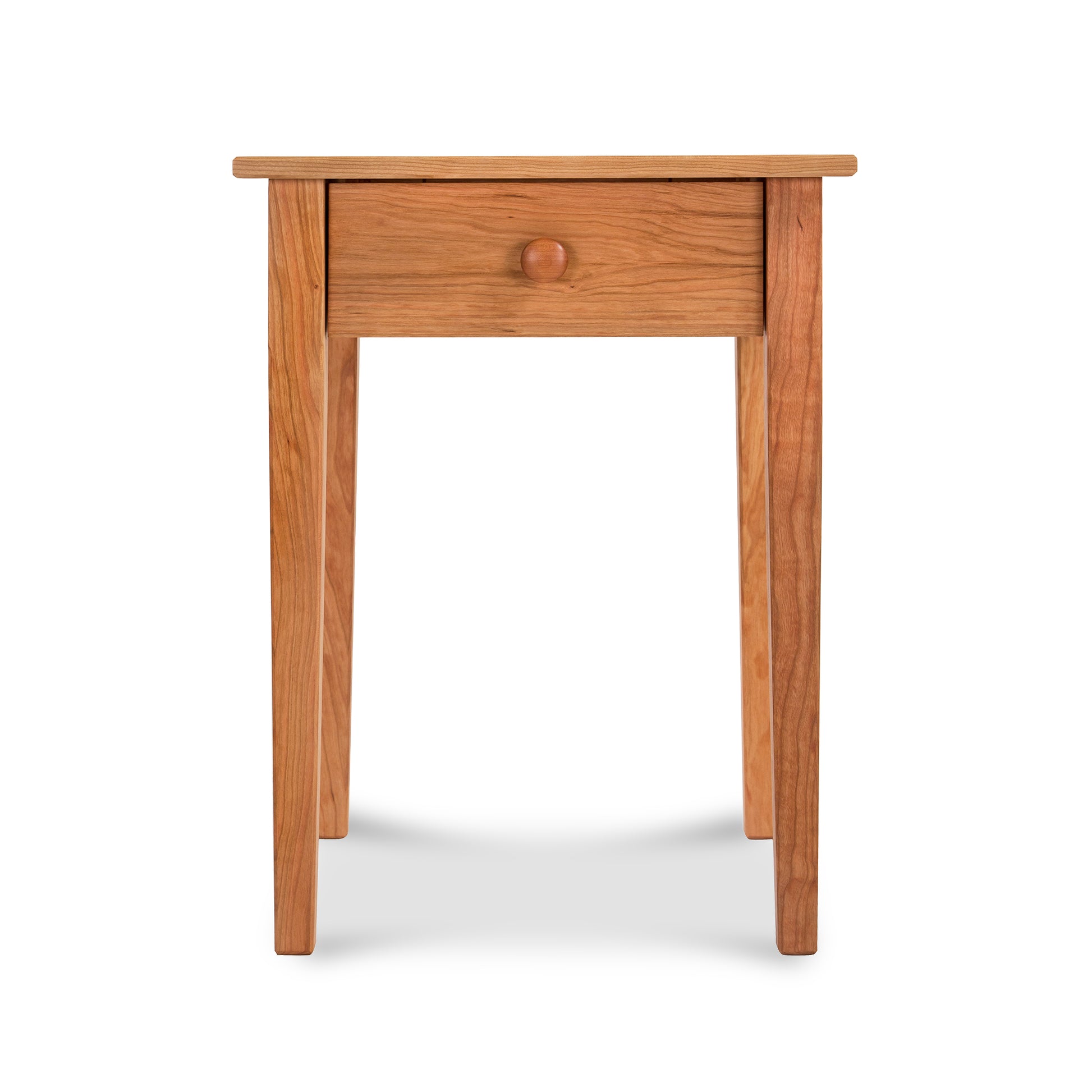 A Vermont Shaker Bedside Table, crafted from sustainably harvested solid woods by Maple Corner Woodworks, with a single drawer and a round knob, standing against a white background. The table features a smooth finish and visible wood grain.