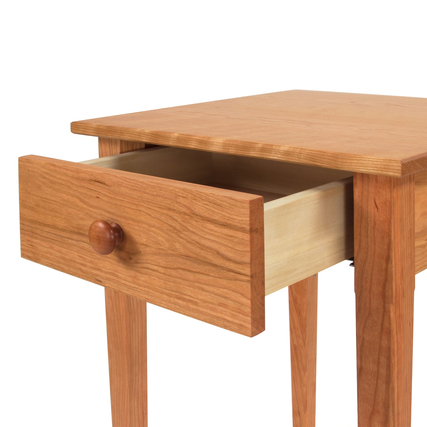 A Vermont Shaker Bedside Table by Maple Corner Woodworks with an open drawer, showcasing its simple design and light wood construction. The knob on the drawer is round, matching the wood’s tone of solid woods.