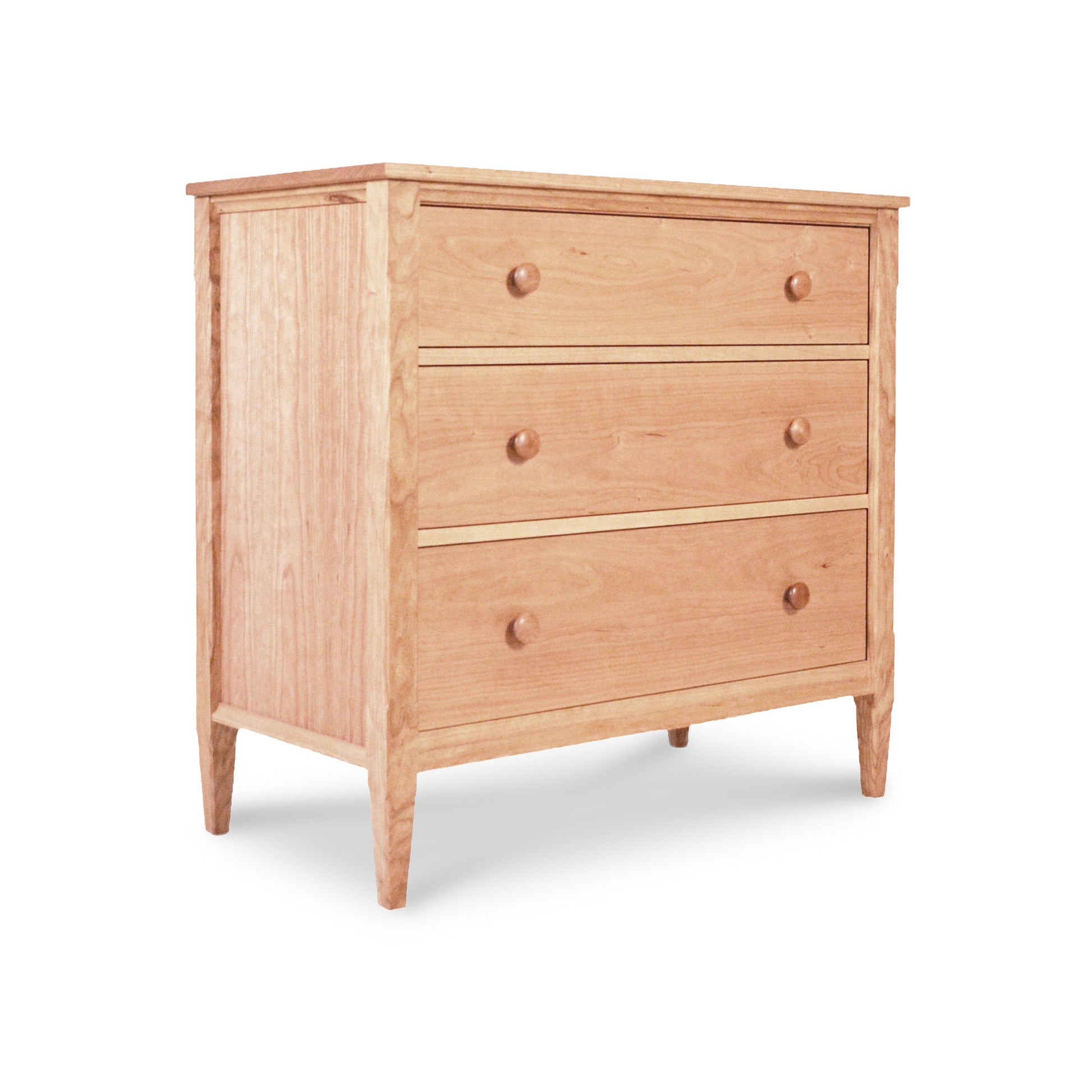 A Vermont Shaker 3-Drawer Chest from Maple Corner Woodworks, with a simple, traditional design, featuring round knobs and standing on short, slightly tapered legs. The background is plain white, highlighting the solid wood finish.