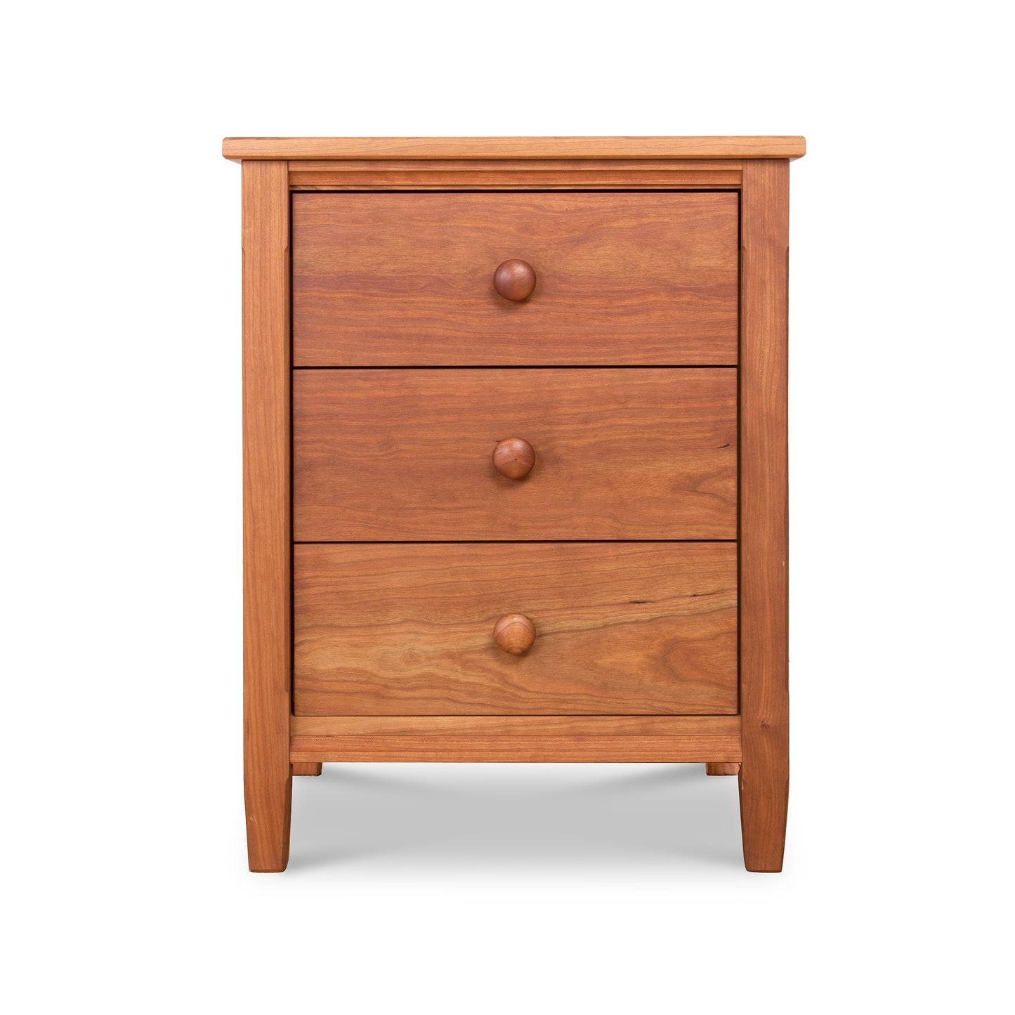 A wooden three-drawer Maple Corner Woodworks Vermont Shaker Nightstand made of cherry wood, featuring round knobs and a simple, sturdy design. The table is isolated on a white background.