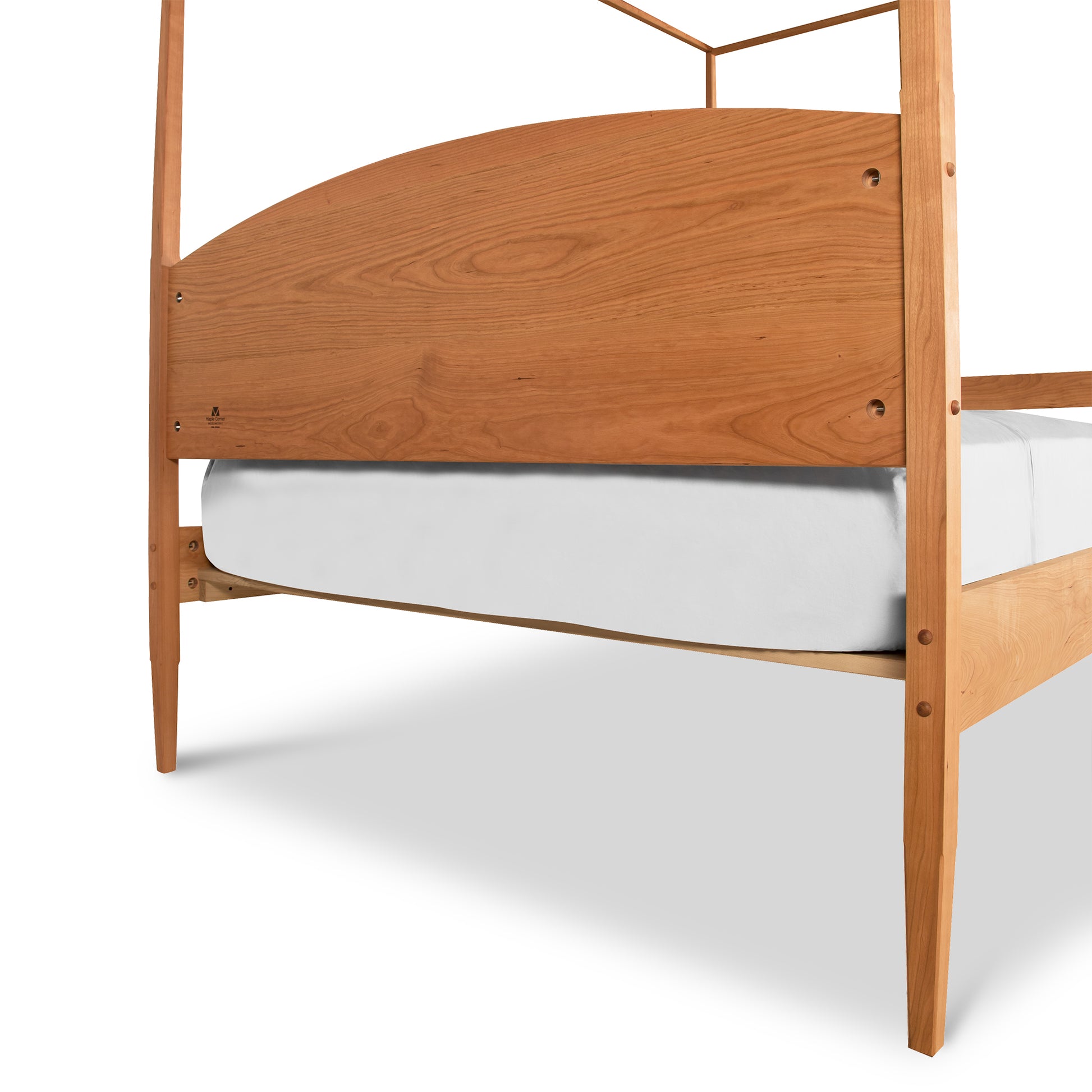A Maple Corner Woodworks Vermont Shaker Four Poster Bed featuring a curved headboard with a visible grain pattern, supporting a white mattress. The structure shows simple, modern craftsmanship.