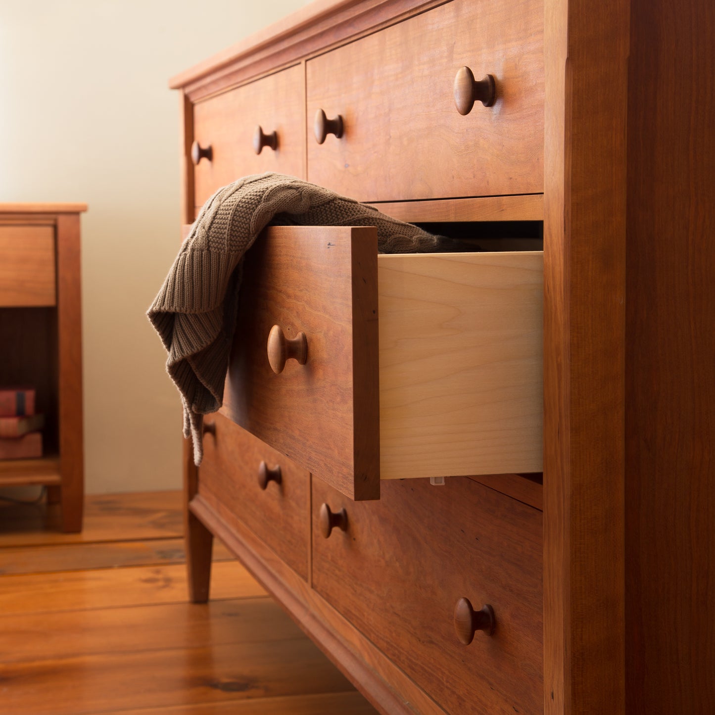 A sturdy Vermont Shaker 6-Drawer Dresser from Maple Corner Woodworks with one open drawer revealing its contents, with a folded grey blanket draped partially out of it, set against a soft background.