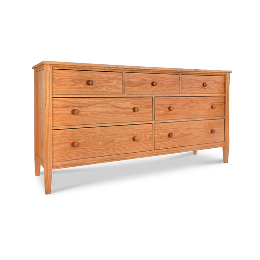 A Vermont Shaker 7-Drawer Dresser from Maple Corner Woodworks, crafted from solid hardwoods, featuring a light brown finish and round handles. It is situated against a white background.