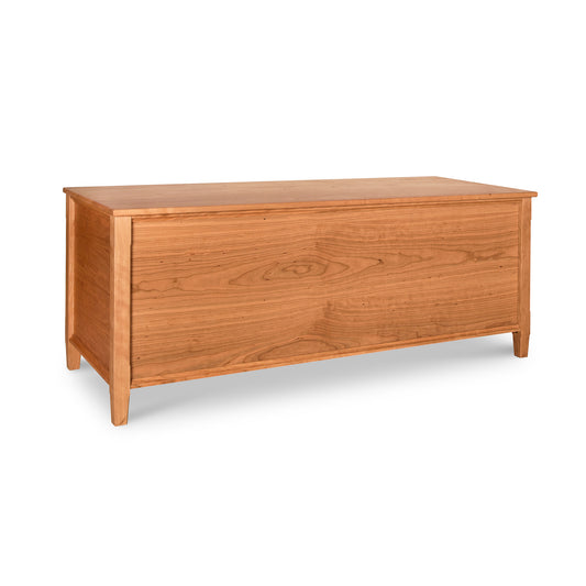 A wooden storage chest, known as the Maple Corner Woodworks Vermont Shaker Blanket Chest, features a hinged top and a simple, rectangular design positioned against a white background. Made from sustainably harvested woods, the