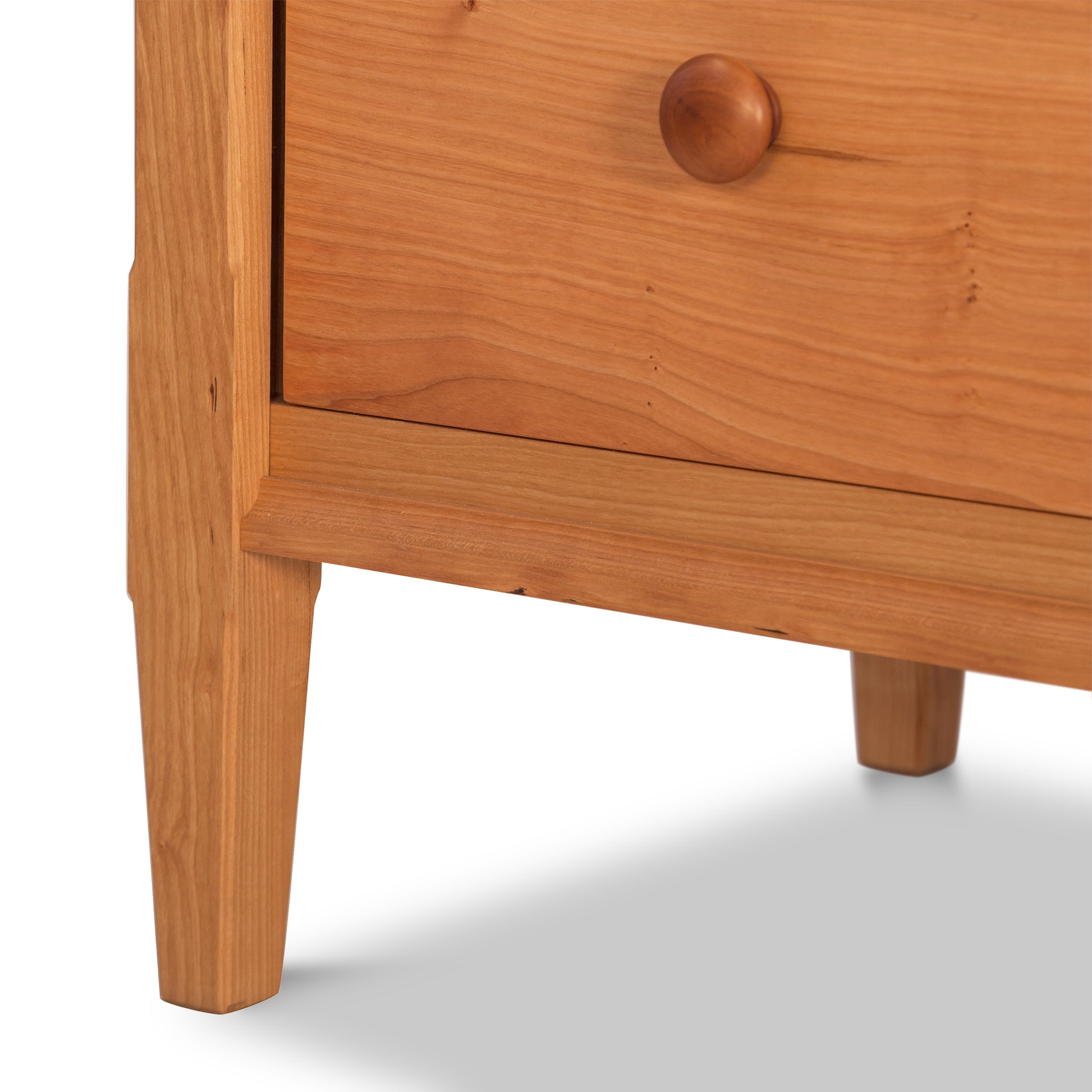 Close-up of a Vermont Shaker Extra Wide Chest by Maple Corner Woodworks featuring a single drawer with a round knob and tapered legs, highlighting the smooth, natural cherry wood grain.
