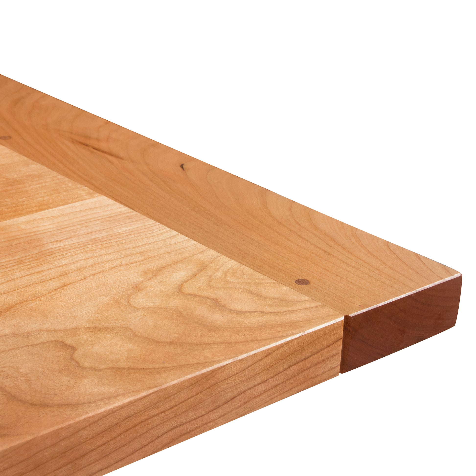 Close-up of a wooden tabletop corner showing the wood grain detail and smooth finish of a Maple Corner Woodworks Vermont Shaker Harvest Extension Dining Table, isolated on a white background.