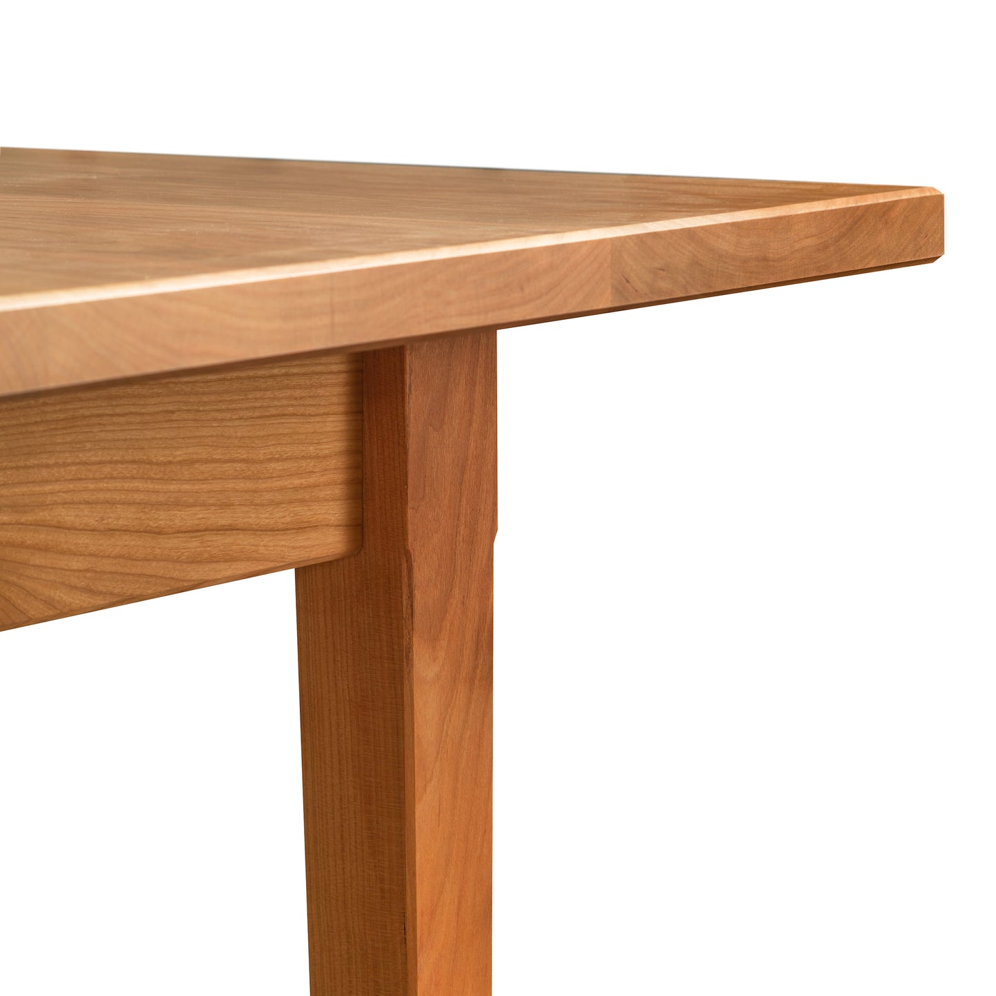 Close-up of a corner of a Vermont Shaker Rectangular Solid Top Dining Table by Maple Corner Woodworks, showing the smooth tabletop and sturdy leg, isolated on a white background.